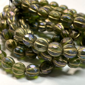 May include: Strands of olive green faceted beads with gold-colored accents. The beads have a ribbed design and a shimmering, iridescent quality. The beads are strung together, creating a necklace or bracelet.