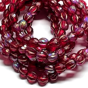 May include: Strands of faceted, deep red beads with iridescent highlights. The beads have a ribbed design and are strung together, creating a layered effect. The beads are likely used for jewelry making or crafting.