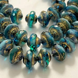 May include: A strand of teal blue and white glass beads with gold accents. The beads are faceted and have a swirl pattern.