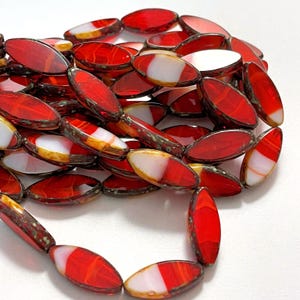 May include: A close-up of a collection of red, oval-shaped beads with white and orange accents. The beads have a glossy finish and are strung together, suggesting a necklace or bracelet. The beads are arranged in a circular pattern.