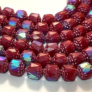 May include: A strand of burgundy glass beads with an iridescent finish. The beads are faceted and have a textured surface.