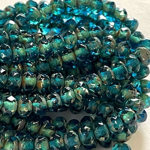 May include: A strand of teal blue glass beads with a speckled, iridescent finish. The beads are faceted and have a round shape.