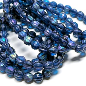 May include: Strands of faceted, dark blue beads with iridescent highlights. The beads have a ribbed texture and are strung together, creating a shimmering effect. The beads are likely used for jewelry making or crafting.