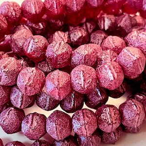 May include: Close-up of a collection of faceted, burgundy-colored beads. The beads have a textured, crackled appearance and are strung together. The beads are likely for jewelry making or crafting.