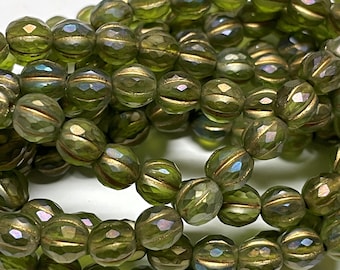 May include: Close-up of olive green faceted beads with gold accents. The beads have a textured, cut-glass appearance and are strung together. The beads are round with a horizontal gold stripe. The beads are suitable for jewelry making.
