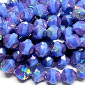 May include: Close-up of a collection of faceted beads in shades of blue and purple. The beads have a unique shape with multiple facets, creating a sparkling effect. The beads are strung together, ready for jewelry making.
