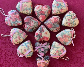 May include: A collection of heart-shaped ornaments with floral patterns. The ornaments feature a cream-colored background with pink and red roses, accented with pink and blue ribbons. Some have white hanging loops.