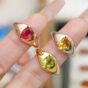 May include: Three gemstone rings with oval-cut stones. One ring has a red ruby, another a yellow citrine, and the third a green peridot. The rings have gold and silver bands.