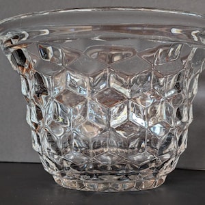 May include: A clear glass bowl with a geometric honeycomb pattern. The bowl has a wide, slightly flared rim and a textured exterior. The design creates a play of light and shadow, enhancing its visual appeal. The bowl is likely used for decorative or serving purposes.