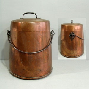 May include: A copper bucket with a lid and a handle. The bucket is cylindrical with a slightly wider base and a curved handle. The lid has a small handle. The bucket is made of copper and has a shiny finish.
