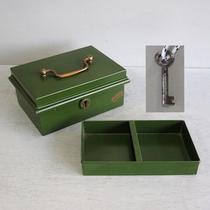 May include: A rectangular olive green metal cash box with a brass-coloured handle on the lid and a keyhole on the front. The box includes a removable interior tray with two compartments and a separate metal key attached to a white and black cord.