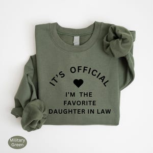 May include: A green sweatshirt with the text "It's Official I'm the Favorite Daughter in Law" in black lettering with a heart.
