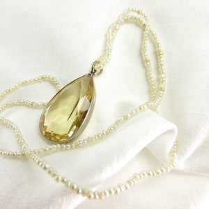 May include: A delicate pearl necklace with a large, faceted, teardrop-shaped yellow gemstone pendant.
