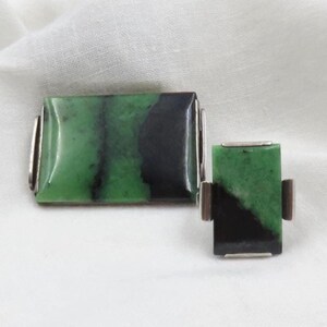 Pode incluir: Um conjunto de joias a condizer com pedras de jade retangulares com tons de verde e preto. As pedras s&atilde;o engastadas em metal prateado. O conjunto inclui uma pe&ccedil;a retangular maior e outra menor.