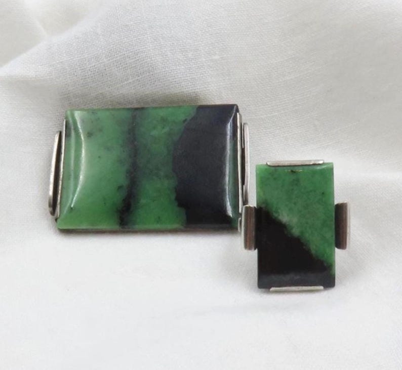 Pode incluir: Um conjunto de joias a condizer com pedras de jade retangulares com tons de verde e preto. As pedras s&atilde;o engastadas em metal prateado. O conjunto inclui uma pe&ccedil;a retangular maior e outra menor.