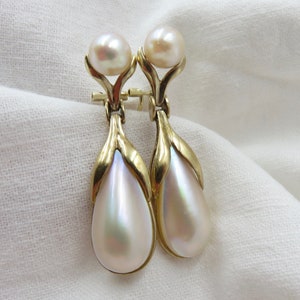 Pode incluir: Um par de brincos de gota em tom dourado com pérolas brancas peroladas em forma de lágrima.