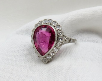 May include: A pear-shaped pink gemstone ring with a halo of smaller diamonds set in platinum.