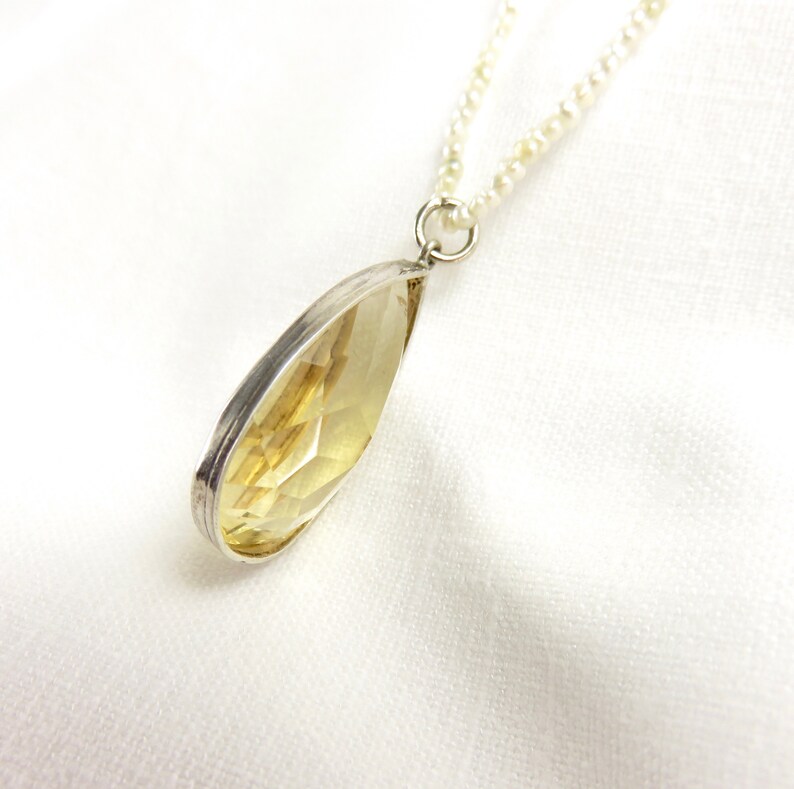 May include: A silver necklace with a teardrop-shaped yellow gemstone pendant. The necklace is made of small white beads.