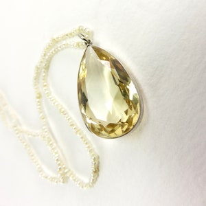 May include: A teardrop-shaped yellow gemstone pendant on a pearl necklace. The pendant is set in silver.