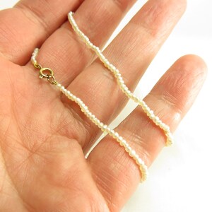 May include: A delicate white pearl necklace with a gold clasp. The necklace is made of small, uniform pearls and is approximately 18 inches long.