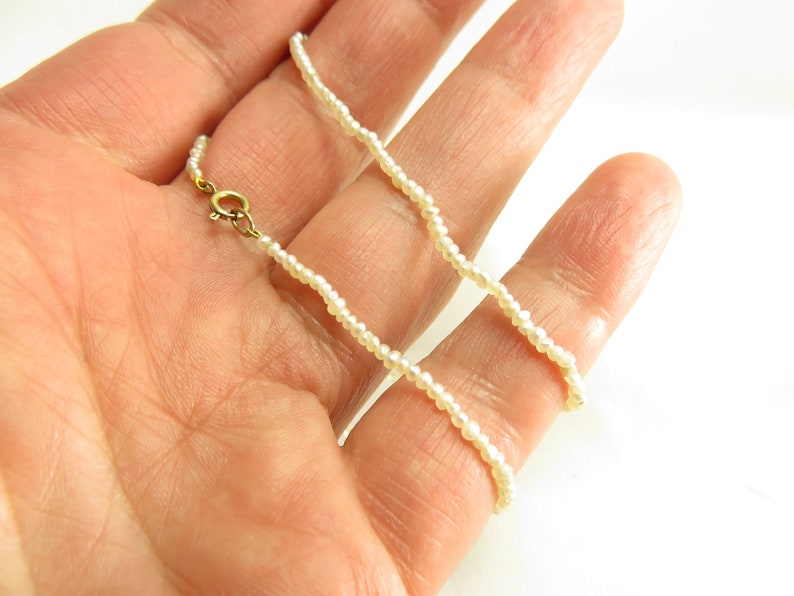 May include: A delicate white pearl necklace with a gold clasp. The necklace is made of small, uniform pearls and is approximately 18 inches long.