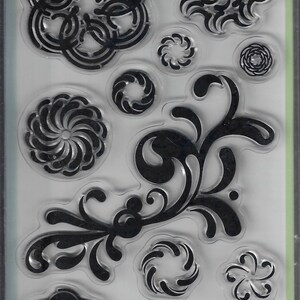 May include: A package of 12 clear stamps featuring various black floral and circular geometric designs. The packaging includes the text 99555, 12 clear stamps, étampes transparentes, and the Inkadinkado logo at the top of the plastic sheet.