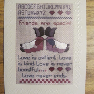 May include: Cross-stitch artwork with the text "Friends are special" and "Love is patient, Love is kind, Love is never boastful, Love never ends." The artwork features two figures and decorative hearts.