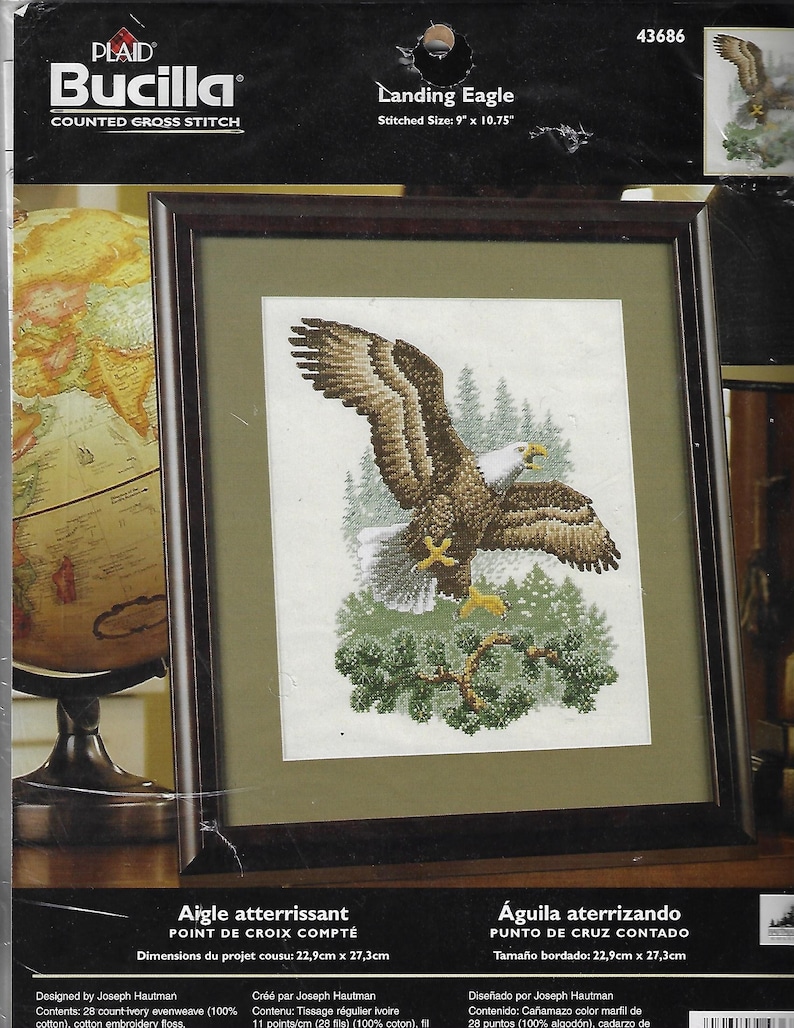May include: Framed cross-stitch kit featuring a detailed image of a bald eagle landing. The eagle, with brown and white feathers, is set against a backdrop of evergreen trees. The stitched size is 9" x 10.75". The kit is labeled "Landing Eagle".