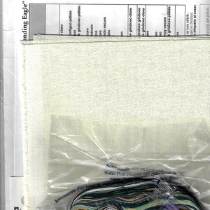 May include: A cross-stitch kit featuring a cream-colored fabric, a variety of colorful threads, and a needle. The kit includes a chart with color codes and the text "Standing Eagle" and "Bucilla Colors".