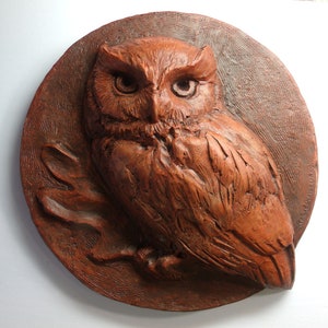 May include: A brown ceramic wall sculpture of an owl perched on a branch. The owl is depicted in a realistic style with detailed feathers and a textured surface.