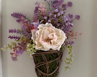 Elegante arreglo floral de pared con peonías color crema y detalles en lavanda.