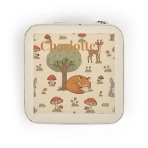 May include: A cream-coloured, square jewellery case with a zip. It displays a woodland scene with a sleeping fox, deer, mushrooms, and the name "Charlotte" in orange. The design has a whimsical, storybook aesthetic, perfect for storing jewellery.