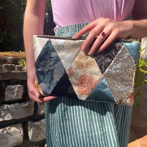 Peut inclure: Une pochette de soirée en patchwork avec une variété de tissus, dont du velours, des paillettes et des imprimés floraux. La pochette est dotée d'une fermeture éclair et d'un tirette de fermeture éclair dorée.