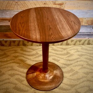 May include: A round wooden table with a dark brown finish. The table has a single pedestal base with a flared bottom.