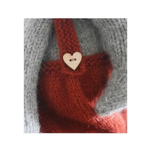 K&ouml;nnte beinhalten: Ein rotes Strickkleid mit einem herzf&ouml;rmigen Holzknopf. Das Kleid hat einen grauen Strickbesatz.