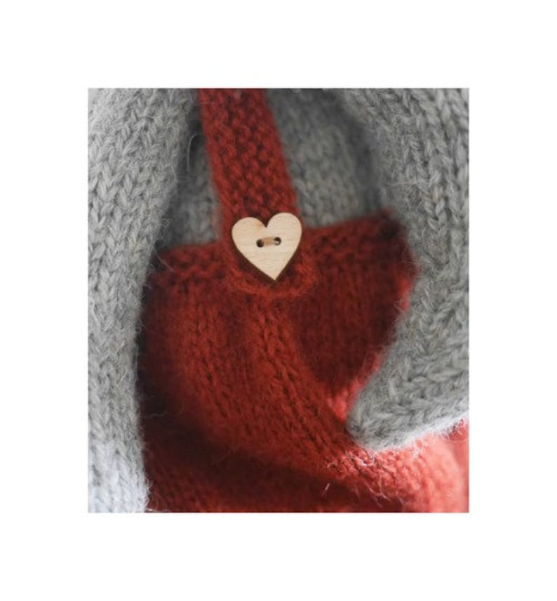 K&ouml;nnte beinhalten: Ein rotes Strickkleid mit einem herzf&ouml;rmigen Holzknopf. Das Kleid hat einen grauen Strickbesatz.