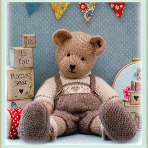 Op de afbeelding: Een gebreide teddybeer met lichtbruine vacht, gekleed in een crèmekleurige trui en een donkerbruine tuinbroek. De beer heeft zwart geborduurde ogen en een neus. Daarnaast staan houten blokken met de tekst R is for ROMEO Bear en een hartje.