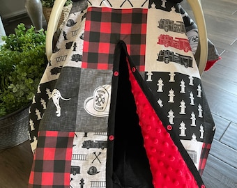 Peut inclure: Une housse de siège auto pour bébé avec un motif patchwork comprenant du carreau de buffle rouge et noir, des camions de pompiers, des bouches d'incendie et un dalmatien. L'intérieur est doublé d'un tissu rouge à picots. La housse est fixée à un siège auto Graco.