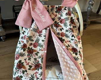 Può includere: Una copertura per seggiolino auto per bambini con un motivo floreale bordeaux, rosa e verde. La copertura ha un fiocco rosa a pois bianchi e il nome "Haven Lee" ricamato. L'interno è in morbido tessuto rosa a pois.