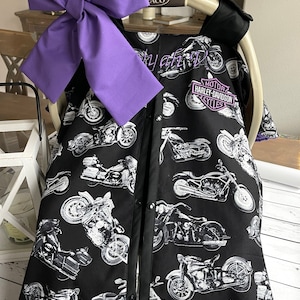 May include: Black and white motorcycle-themed baby car seat cover with a large purple bow. The cover features a pattern of various motorcycle illustrations and the Harley-Davidson Cycles logo.