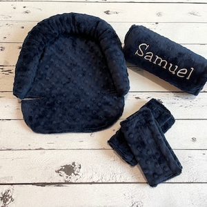 May include: Navy blue baby car seat headrest, shoulder strap covers, and a bolster pillow. The bolster pillow is embroidered with the name "Samuel" in white thread. All items have a textured, dotted pattern.