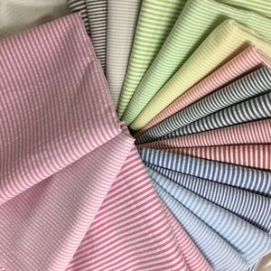 May include: A collection of seersucker fabric in various colors, including pink, green, blue, and brown. Each fabric has a striped pattern. The fabrics are arranged in a circular fan shape.
