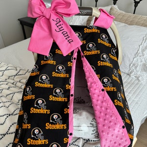May include: A black and yellow Steelers-themed baby car seat cover with a pink bow and trim. The cover features the Steelers logo and text. The name "Aiyana" is embroidered on the bow. The interior is a soft pink fabric.