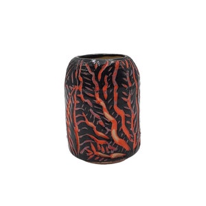 Peut inclure: Un vase cylindrique en céramique avec une base noire et un motif de dessins rouges verticaux en forme de branches. Le vase a une surface légèrement texturée et un intérieur sombre. L'esthétique générale est moderne et artistique.