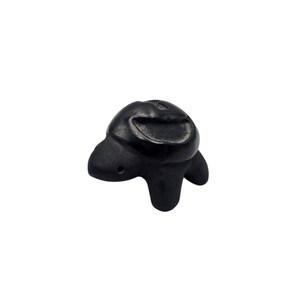 May include: A small, black turtle figurine with a smooth, polished finish. The turtle has a rounded shell, a small head, and stubby legs. The figurine is made of a solid, dark material.