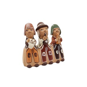 Puede incluir: Figura de cerámica que representa a tres músicos. Cada figura lleva un sombrero y toca un instrumento diferente: un tambor, una flauta y una trompa. Las figuras visten trajes coloridos con patrones geométricos y están conectadas por una base marrón.