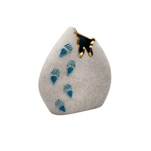 May include: A decorative, teardrop-shaped vase with a textured, light gray surface. The vase features six turquoise paw print designs and a gold-trimmed opening. The interior of the opening is dark blue.