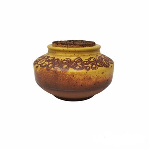 May include: A yellow ceramic jar with a brown cork lid and a brown swirl design around the middle.