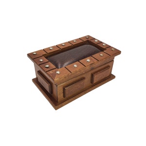 May include: A wooden box with a leather-covered lid and metal accents. The box has a rectangular shape and is made of dark brown wood. The lid is decorated with a pattern of small squares and has a leather lining.