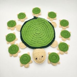 May include: A large circular green crocheted turtle shell with a dark green border, accompanied by a small crocheted turtle head and ten smaller circular green and beige crocheted pieces arranged in a circle around the center.